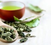 Wooden spoon with dried green tea leaves in it and a cup of green tea on a backstage