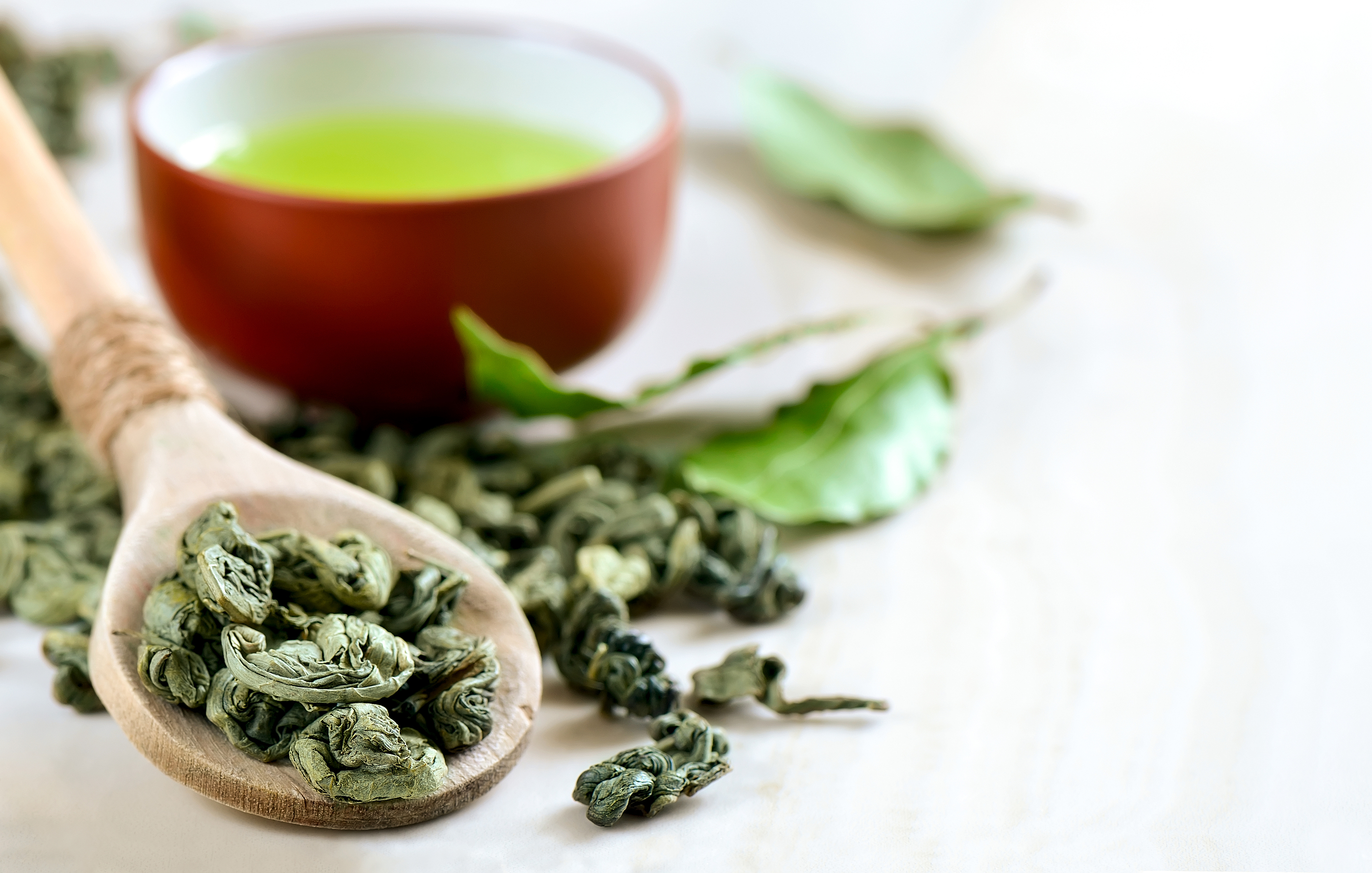 Wooden spoon with dried green tea leaves in it and a cup of green tea on a backstage