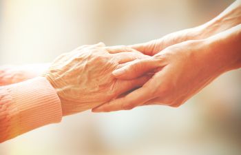 Hands of a young woman holding elderly person's hands.