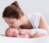 Mother kissing her sleeping newborn on its head.