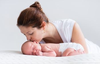 Mother kissing her sleeping newborn on its head.