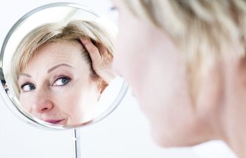 Mature woman looking at her face in a mirror and considering facial Anti-Aging Treatments in Beverly Hills CA