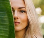 Beautiful woman hiding half of her face behind a palm leaf.