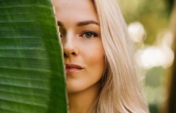 Beautiful woman hiding half of her face behind a palm leaf.