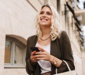 elegant blonde walks the street smiling and holding the phone