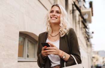 elegant blonde walks the street smiling and holding the phone