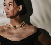 Close up portrait of a beautiful elegant young woman wearing an expensive pearl necklace, pearl earrings in a black evening dress.