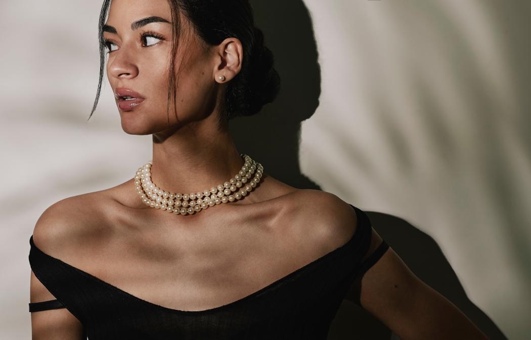 Close up portrait of a beautiful elegant young woman wearing an expensive pearl necklace, pearl earrings in a black evening dress.