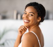 Natural Beauty. Attractive Black Woman Touching Chin And Looking At Camera While Standing In Bathroom At Home, Beautiful African American Female Enjoying Her Smooth Skin After Skincare Routine