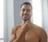 Handsome young hispanic man in a spa salon interior smiling and touching his beard