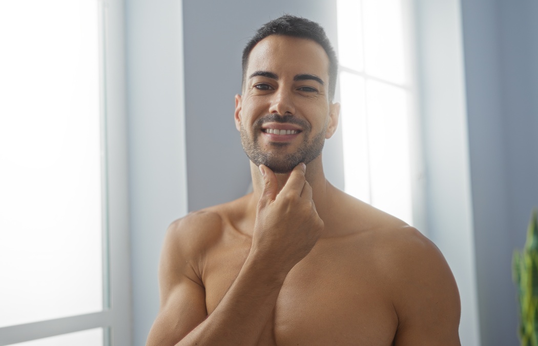 Handsome young hispanic man in a spa salon interior smiling and touching his beard